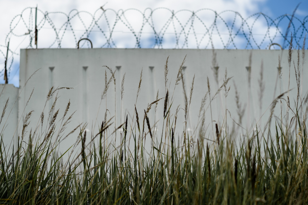 grass with precast concrete fence with barbed wire and sky with clouds