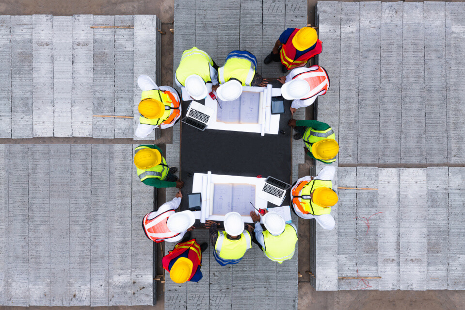 A group of construction workers gathered around design templates for a precast concrete fence.