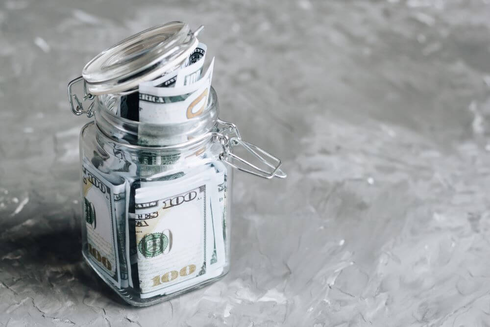 A jar full of money that has been saved, placed on a concrete background.